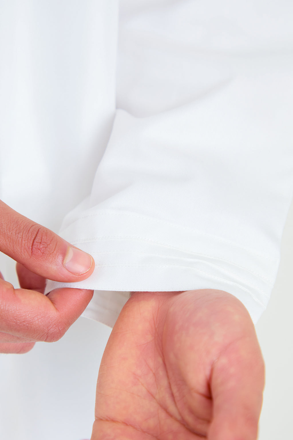 Close-up of a person's hand holding a white fabric with a plain background